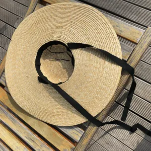 Gros plan du chapeau de paille à très grand bord avec texture tressée et ruban noir.