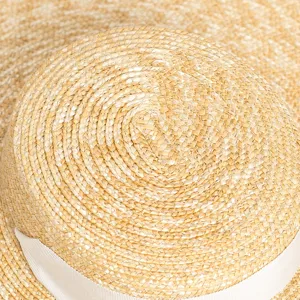 Gros plan sur la couronne du chapeau de paille avec texture tissée et ruban blanc.