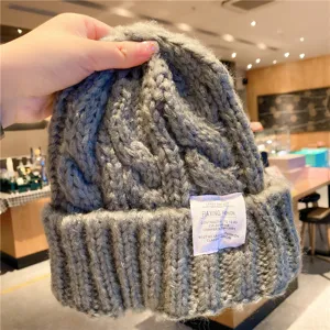 Gros plan du bonnet en tricot gris montrant la texture épaisse torsadée et l'étiquette.