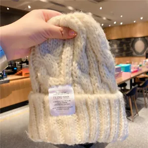 Vue détaillée d'un bonnet en tricot épais beige avec une étiquette tissée et une texture chaude.