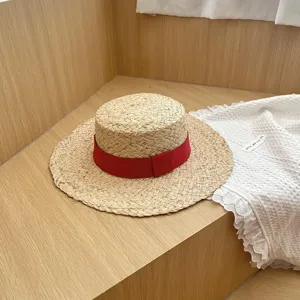 Gedetailleerd opname van een stijlvolle raffia platte strohoed met een rood lint op houten achtergrond.