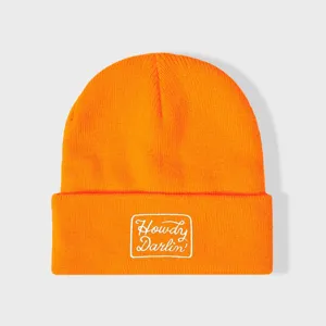 Oranje gebreide muts met omslag en witte geborduurde letterpatch voor stijlvolle winterse warmte.