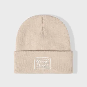 Detail van beige gebreide muts met omslag en het schattige geborduurde Howdy Darlin patch ontwerp.