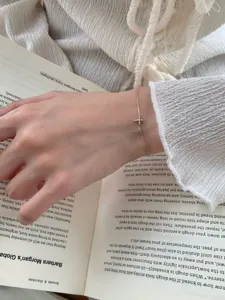 Λεπτομέρεια βραχιολιού με κρυστάλλινο σταυρό, λεπτή χρυσή αλυσίδα και λαμπερό μενταγιόν.