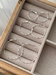 Detailed view of three pairs of silver hoop earrings in graduated sizes, neat jewelry box display.