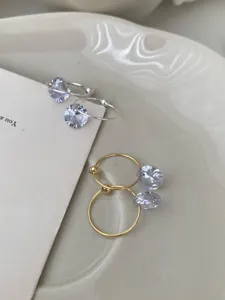 Nahaufnahme von minimalistischen Solitär-Zirkonia-Creolen in Silber und Gold, feines Detail.