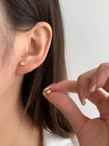 Gros plan de délicates boucles d'oreilles solitaires en or portées avec main.