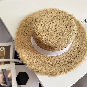 Vista detallada del sombrero de paja con cinta blanca y borde deshilachado, ideal para la playa.