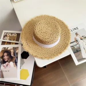 Primer plano de un sombrero de paja de verano con borde deshilachado y cinta blanca.