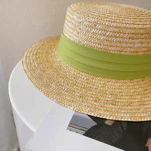 Close up view of summer flat top straw hat with green ribbon detail, natural woven texture.