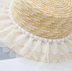 Detail van kinderstrohoed met parelketting en delicate kanten tule randversiering.