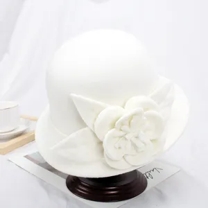 Detailopname van een elegante witte viltmuts met prachtige handgemaakte cameliabloem aan de zijkant.