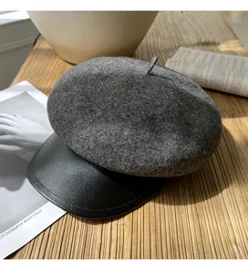 Nahaufnahme einer dunkelgrauen Wollbaskenmütze mit schwarzem Leder-Schirm auf Holztisch.