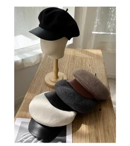 Detailansicht der Wollberette mit Lederkrempe und gestapelten Farben auf Holztisch.
