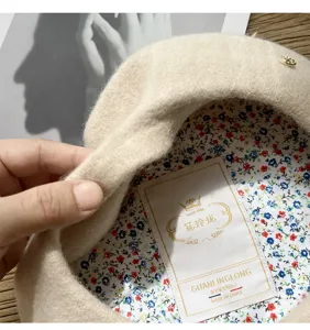 Primer plano de boina de lana beige con elegante forro floral y pequeño detalle metálico.