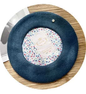 Vista detallada de boina de lana azul oscuro con dije de metal y forro floral para mujer invierno.