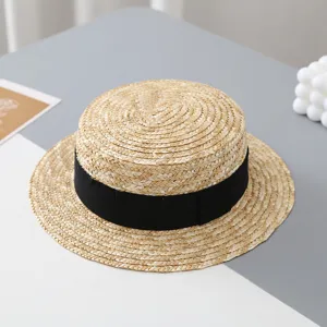 Primer plano de sombrero de paja plano para niños con cinta negra en mesa minimalista.