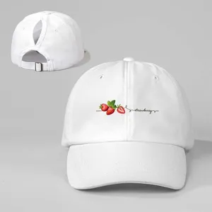 Detail view of white ponytail baseball cap with cute strawberry print and adjustable strap.