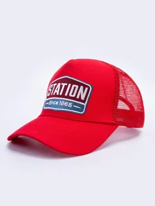 Λεπτομέρεια κόκκινου καπέλου trucker με πίσω μέρος από δίχτυ και κεντημένο λογότυπο.