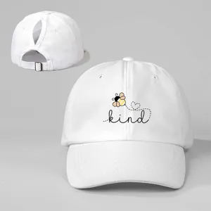 Weiße Baseballkappe mit Pferdeschwanzöffnung, süßem Bienen-Druck und Textdetail für Damen.