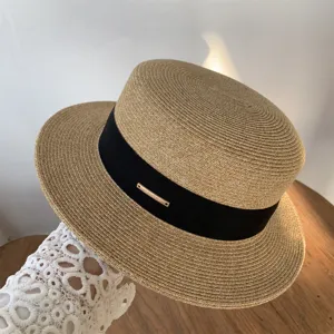 Primer plano detallado de un sombrero de paja de verano para mujer con cinta negra y logo de metal.
