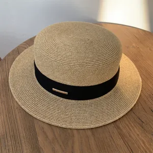 Vista detallada del sombrero de paja minimalista con cinta negra y detalle dorado.