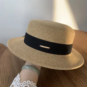 Primer plano de un sombrero de paja de verano con cinta negra y placa de logotipo.