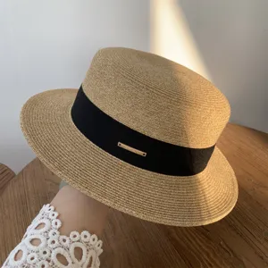 Vista detallada del sombrero de paja con textura fina, cinta negra y adorno metálico elegante.