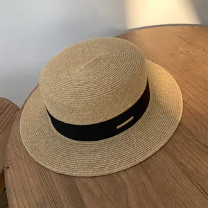 Vista detallada de un sombrero de paja plano clásico con cinta negra en mesa de madera.