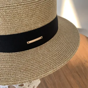 Vista detallada de sombrero de paja plano para mujer con cinta negra y etiqueta, verano playa.
