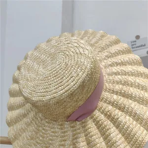 Primo piano dettagliato di un cappello di paglia a tesa larga con nastro rosa e bordo ondulato.