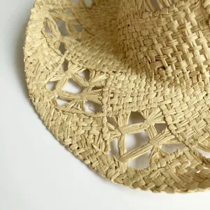 Close-up detail of woven raffia straw hat showing delicate cutout pattern texture.