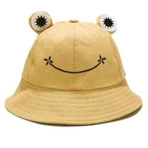 Close-up detail of cute frog bucket hat with smiling face embroidery and 3D frog eyes.