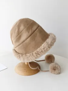 Close-up detail of the plush trimmed winter bucket hat showing soft suede texture and pom-poms.