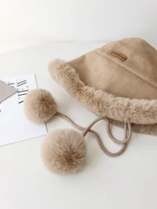 Close-up detail of cozy winter plush bucket hat with fluffy pom-pom ties and soft suede finish.