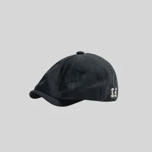 Vista detallada de la gorra estilo newsboy oscura, mostrando su diseño clásico y número lateral.