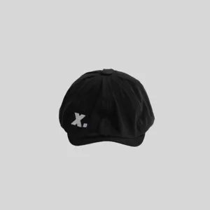 Vista detallada gorra plana negra con bordado X blanco, boina de pintor estilo retro.