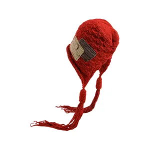 Detailed view of the cute red knit earflap hat with braids, tassels, and side patch accents.