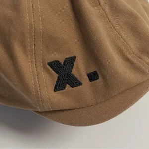 Vista detallada gorra plana de lona, boina marrón con logotipo bordado negro, sombrero estilo