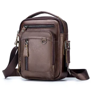 Brown leather texture close-up with metal zipper pockets and adjustable canvas shoulder strap.