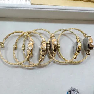 Dettaglio dell'orologio da polso in filo d'acciaio dorato con design a cavo intrecciato unico.