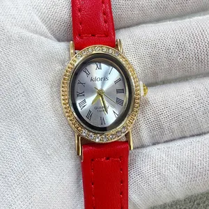 Detail view of red leather strap quartz watch with sparkling oval rhinestone gold bezel.