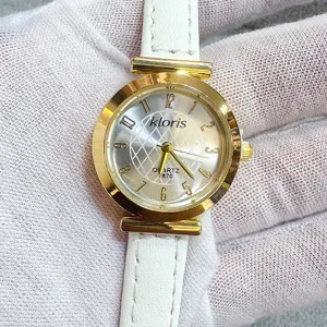Kloris women quartz watch detail featuring round gold dial, white leather strap and numbers.