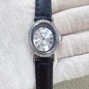 Kloris women quartz watch detail, elegant oval rhinestone dial with black leather strap.