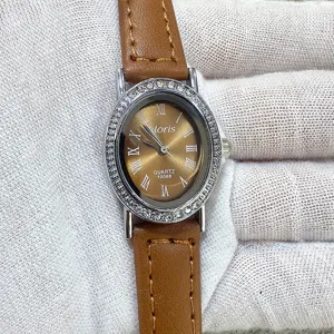 Detail view of elegant oval rhinestone quartz watch with brown leather strap and Roman numerals.