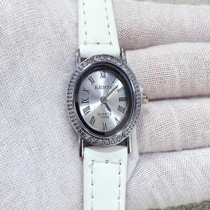 Kloris women quartz watch detail view, elegant oval rhinestone bezel with white leather strap.