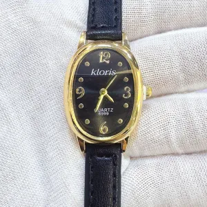 Nahaufnahme Detail einer Damen Quarzarmbanduhr mit ovalem Goldgehäuse und schwarzem Lederarmband.