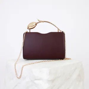 Burgundy hard case clutch bag with elegant gold floral handle and chain strap for women.