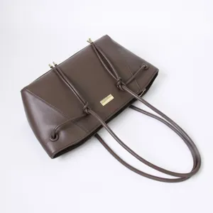 Brown leather shoulder bag detail view with knotted straps and decorative metal hardware.