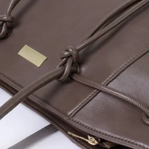 Brown leather tote bag detail featuring elegant knotted handles and polished metal hardware accent.